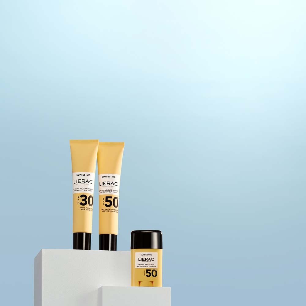 Drei Sonnenpflegeprodukte: zwei Tuben SPF30 und SPF50, eine Stick SPF50. Marke LIERAC. Auf weißem Podest.