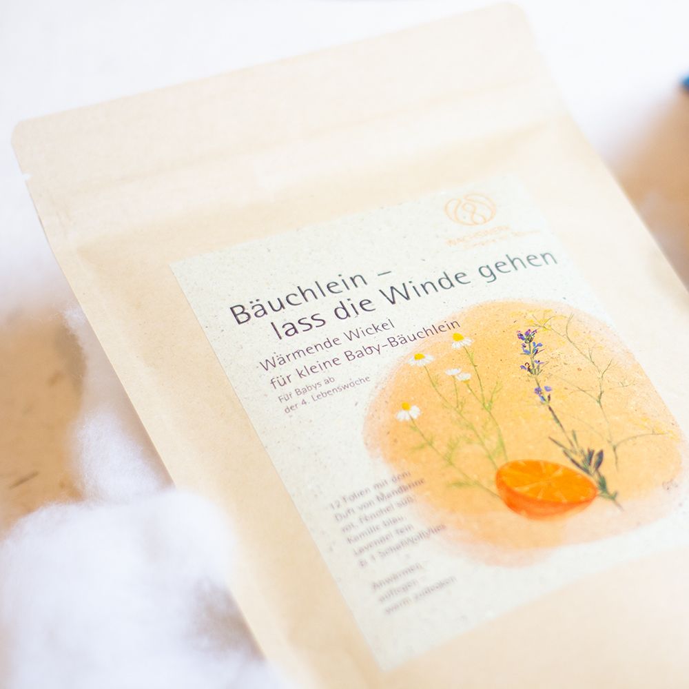 Nahaufnahme einer beige Papiertüte mit Aufkleber, der Kräuter und eine Orange zeigt. Produkt: Bäuchlein - lass die Winde gehen.