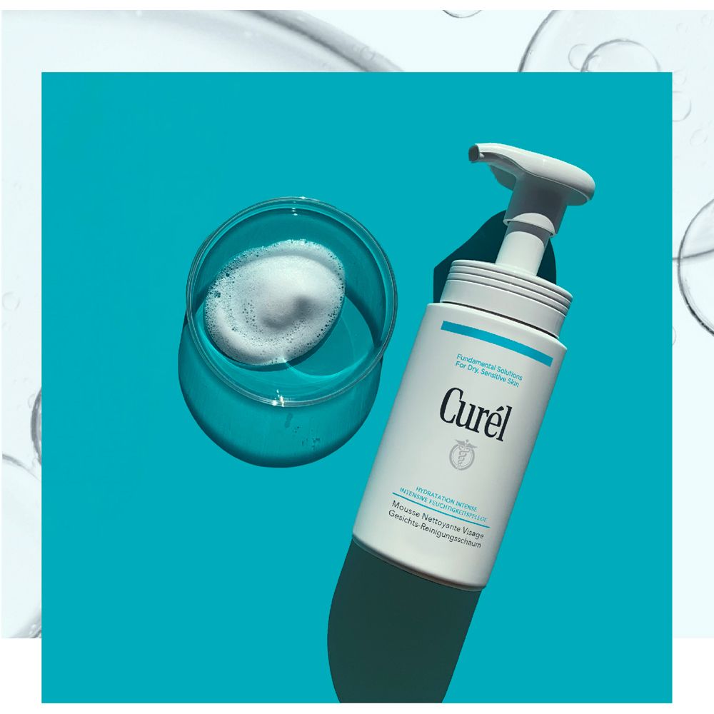 Weißer Spender mit Schaum in einem Glas. Aufschrift: Curél, Mousse Nettoyante Visage. Blauer Hintergrund.