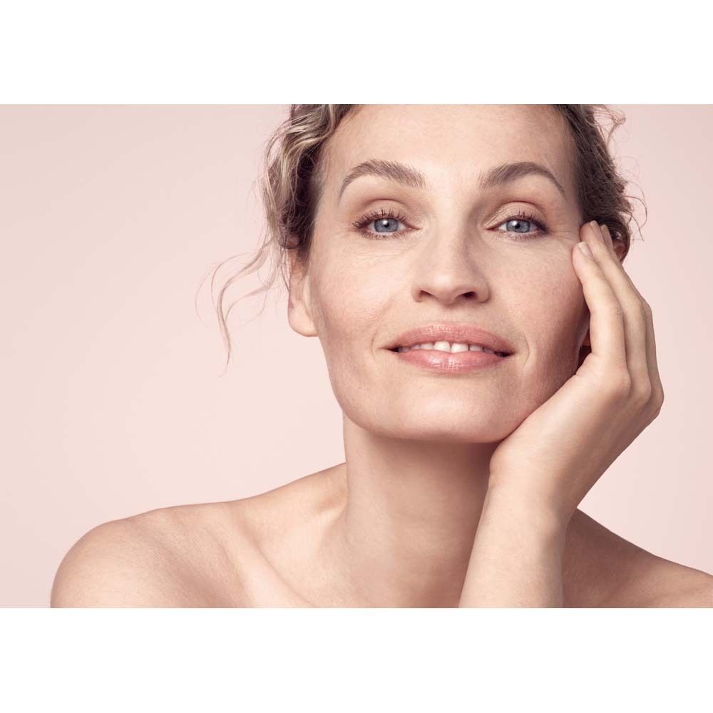 Porträt einer Frau mit leicht geröteter Haut. Sie berührt sanft ihre Wange.  Im Hintergrund ein rosafarbener Farbverlauf.