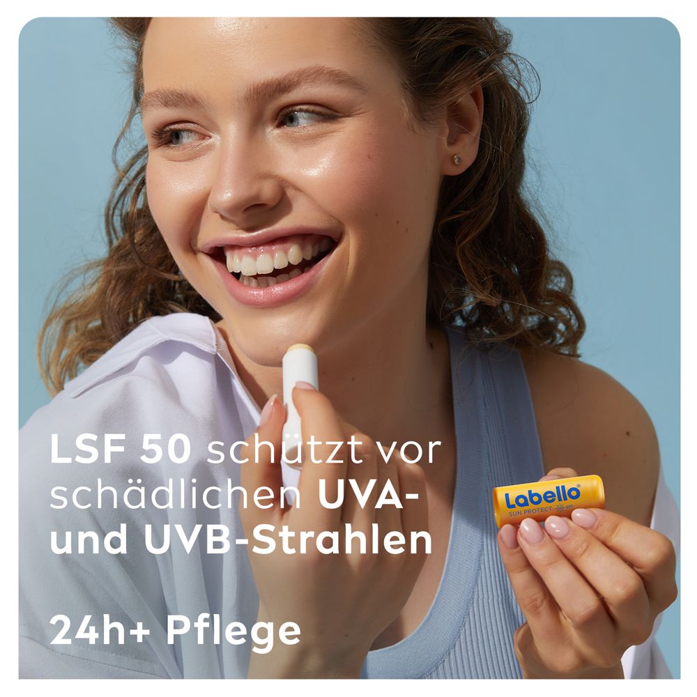 Junge Frau trägt Labello SUN PROTECT auf die Lippen auf, hält den Lippenpflegestift in der Hand.