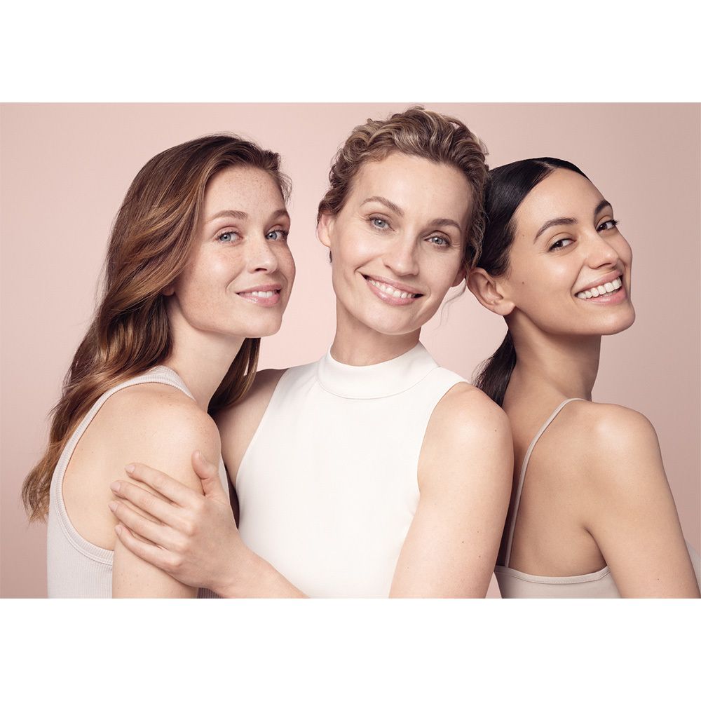 Drei Frauen lächeln in die Kamera. Sie tragen helle Oberteile. Hintergrund ist rosa.