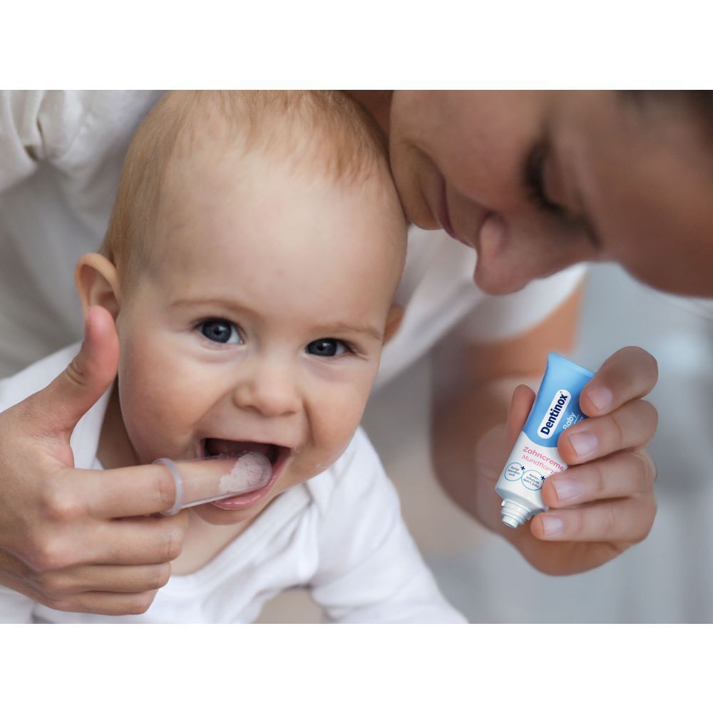 Baby bekommt Zahncreme auf den Finger. Mutter oder Vater putzt dem Baby die Zähne mit Fingerzahnbürste.