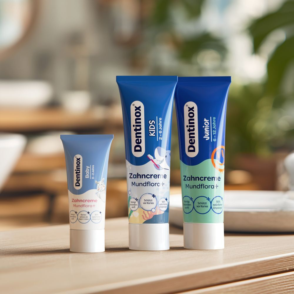 Drei Zahncreme-Tuben. "Dentinox Baby", "KIDS" und "Junior". Alle blau, mit Produktnamen.