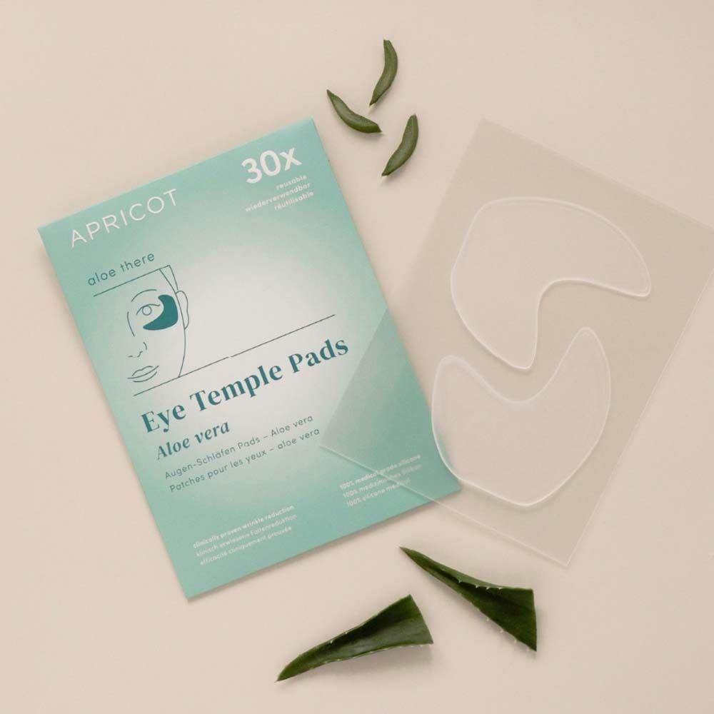 Verpackung und Pads von APRICOT Eye Temple Pads. Aloe Vera. Pads und Aloe Vera Blätter liegen daneben.