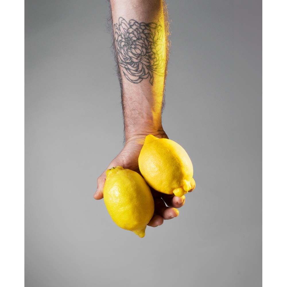 Hand mit zwei Zitronen. Arm mit Tattoo im Hintergrund. Gelber Hintergrund.