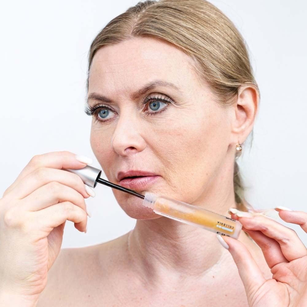 Frau trägt Serum mit Applikator auf die Lippen auf. Fläschchen sichtbar. Gesicht nah.