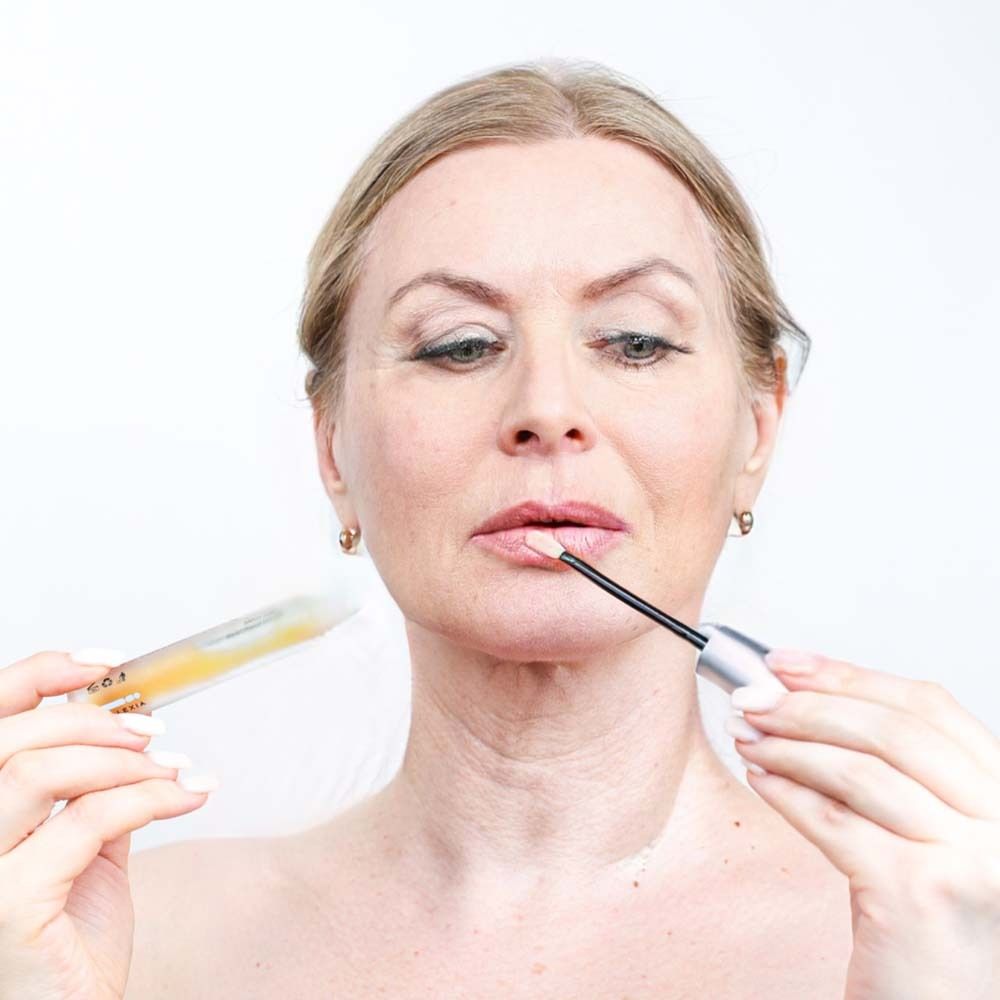Frau trägt Serum mit Applikator auf die Lippen auf. Fläschchen und Applikator sichtbar. Nahaufnahme.
