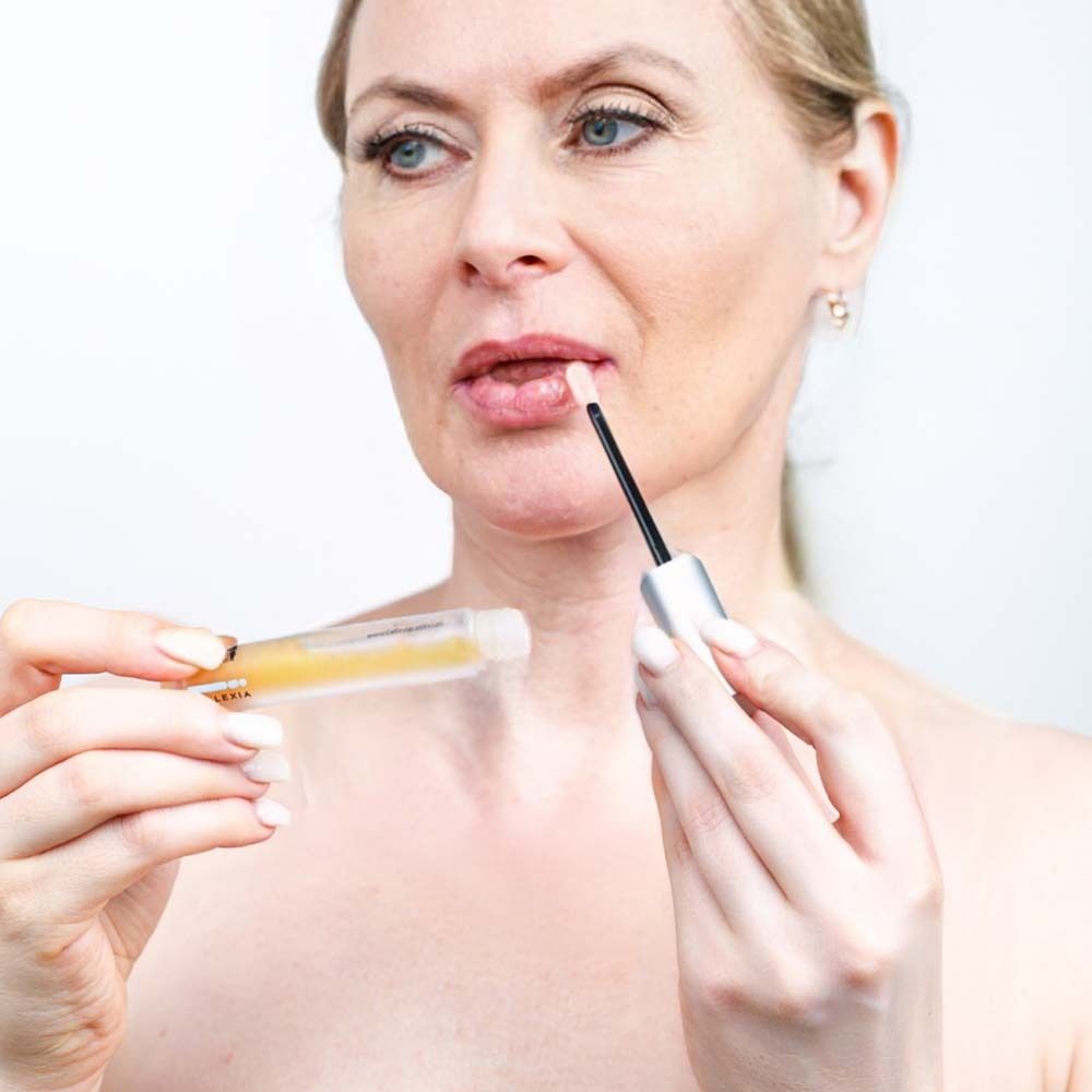 Frau trägt Serum mit Applikator auf die Lippen auf. Fläschchen und Applikator sichtbar. Nahaufnahme.
