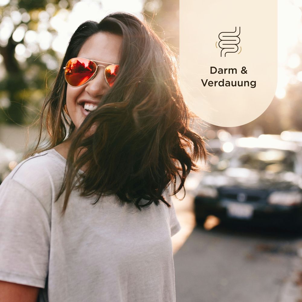 Lächelnde Frau mit Sonnenbrille. Hintergrund: Straße, Autos. Text: Darm & Verdauung.