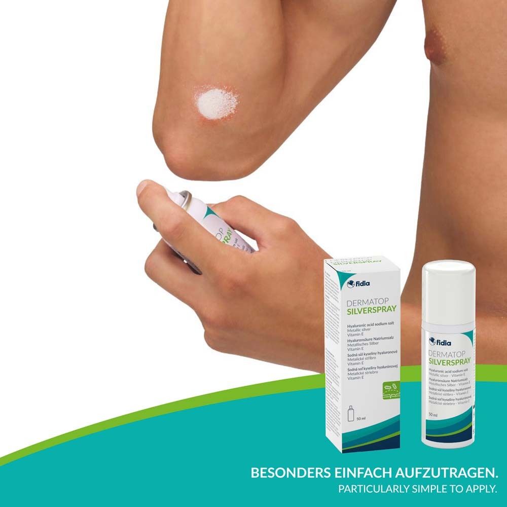 Person sprüht Dermatop Silverspray auf den Ellenbogen. Flasche und Verpackung im Hintergrund.