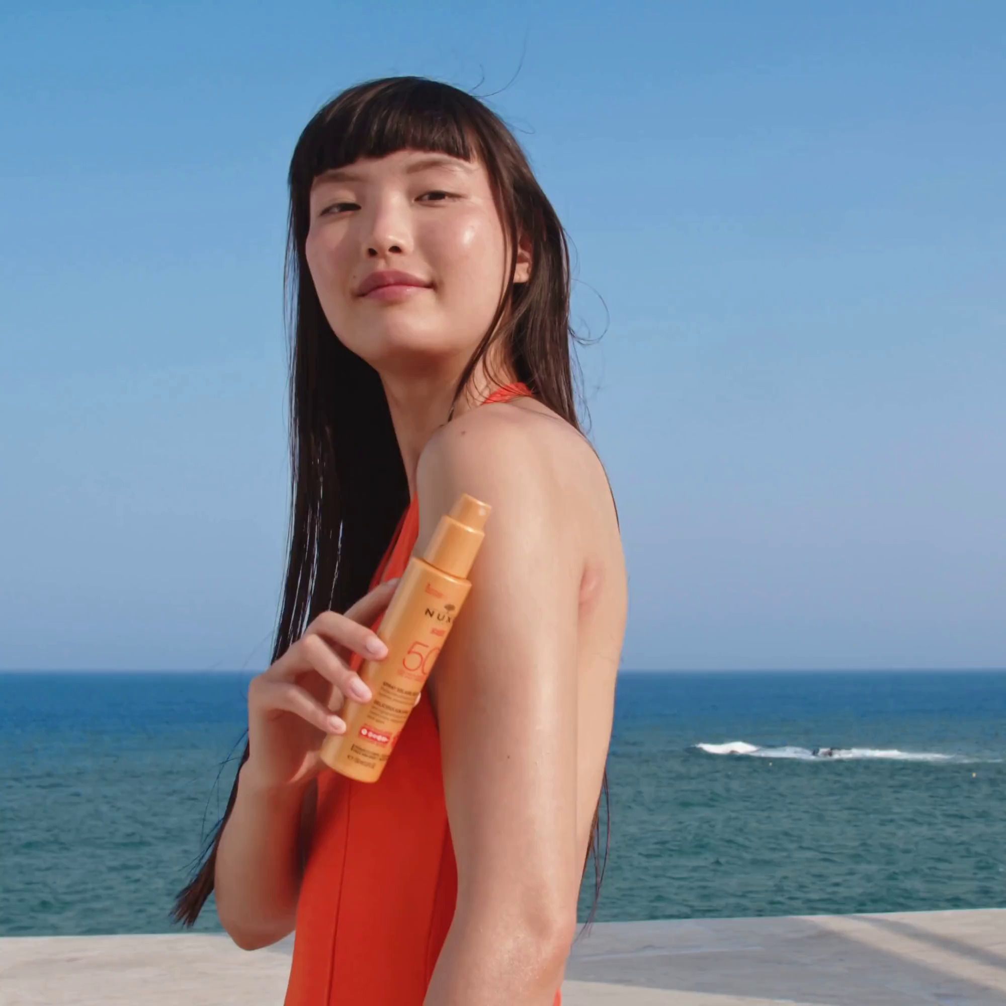Frau hält Sonnenspray am Strand. Meer im Hintergrund.