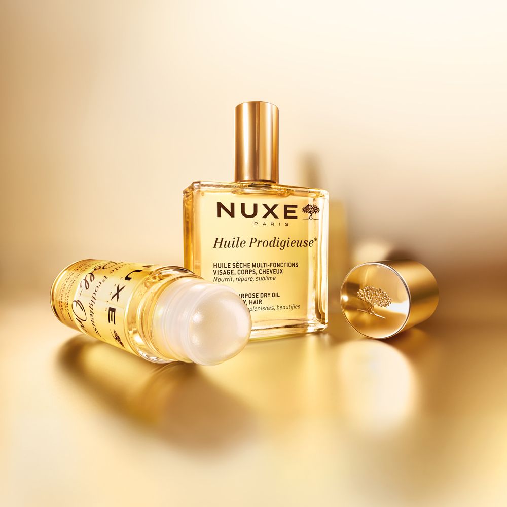 NUXE Huile Prodigieuse und Roll-on. Goldene Flaschen, goldener Hintergrund. Geöffnete Kappe.