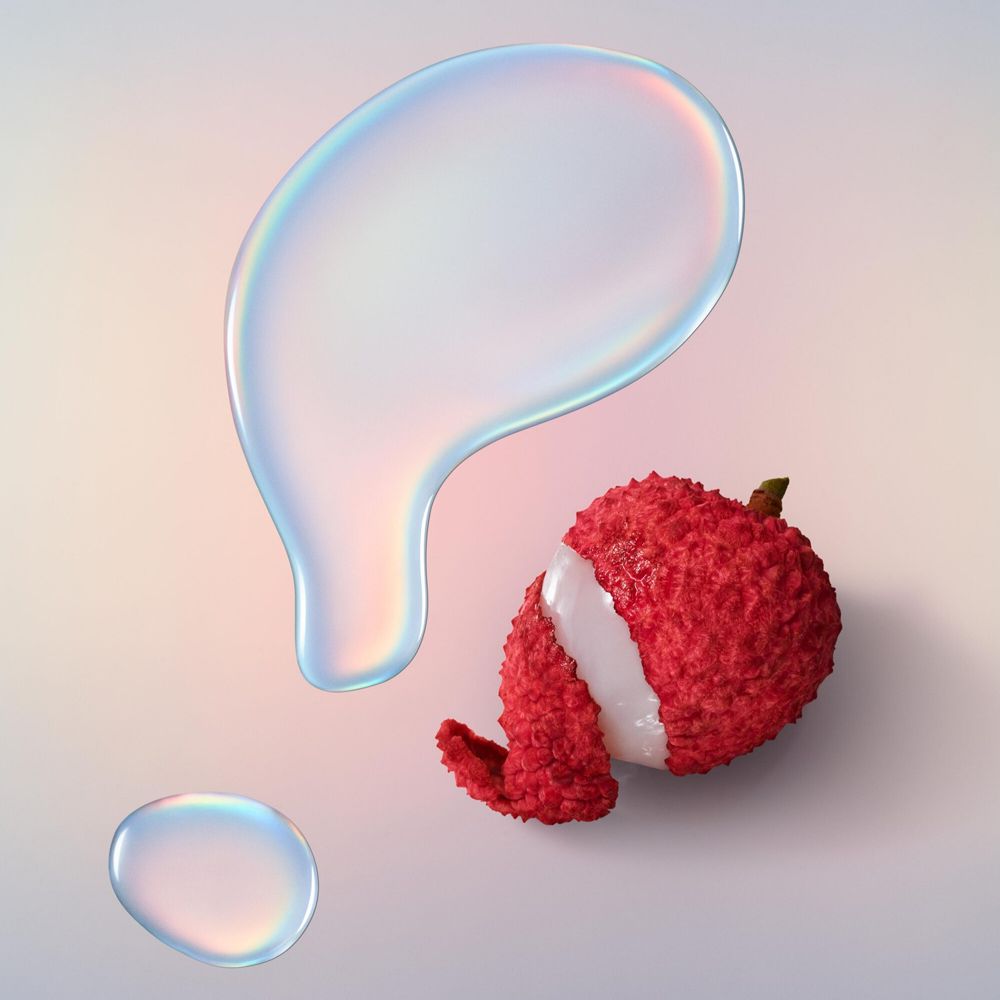 Zwei Tropfen und eine Litschi-Frucht. Tropfen sind durchsichtig. Litschi rot mit weißem Fruchtfleisch.