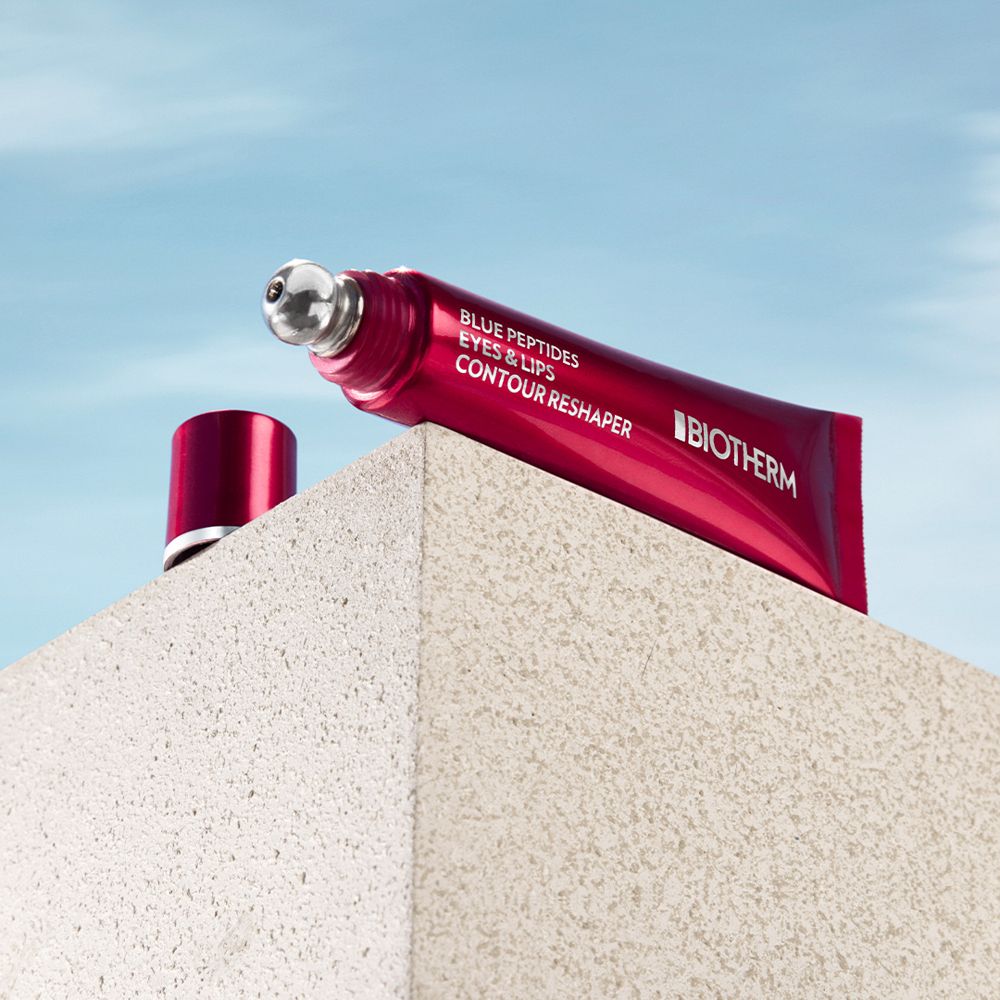 Rote Tube mit Applikator. BIOTHERM Blue Peptides Eyes & Lips Reshaper. Liegt auf einer Oberfläche.