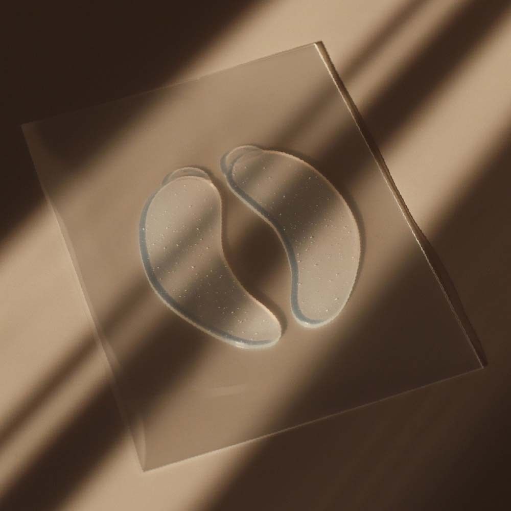 Zwei transparente Eye Pads auf einer transparenten Oberfläche. Sie liegen leicht schräg im Licht.
