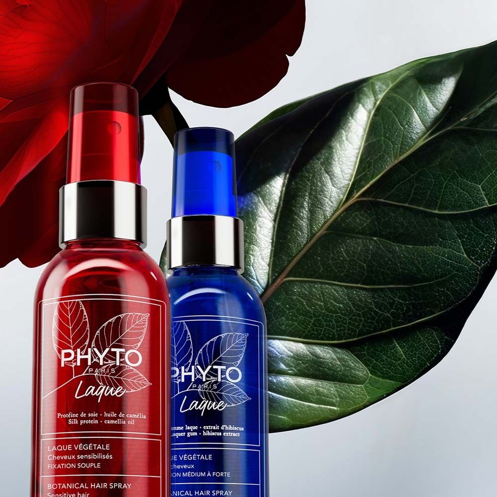 Zwei Haarspray-Flaschen, rot und blau, neben einem Blatt und einer roten Blüte. Aufschrift PHYTO PARIS, LAQUE. Botanisches Haarspray.