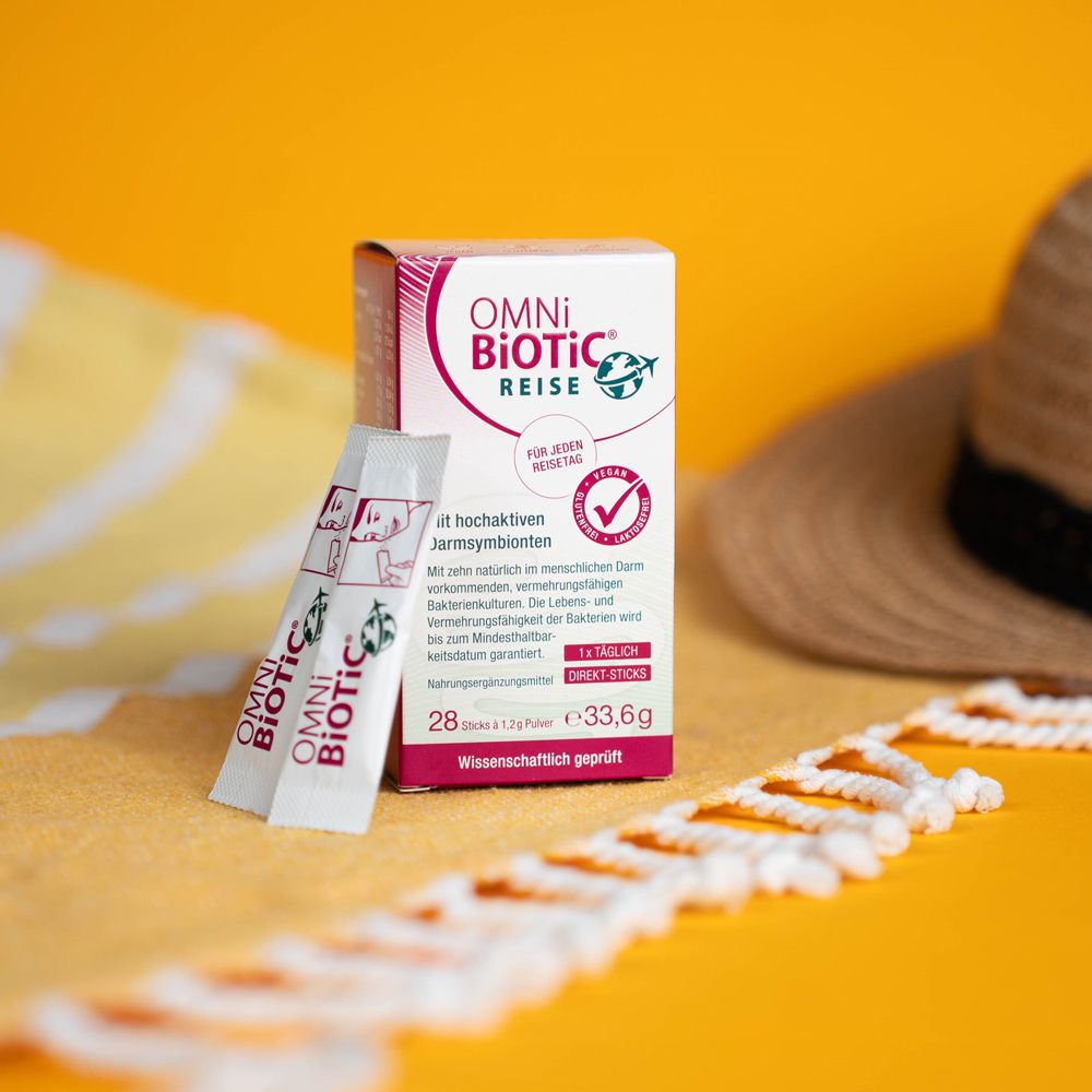 OMNi-BiOTiC REISE Direkt-Sticks und Verpackung auf gelbem Untergrund. Zwei Sticks liegen daneben.