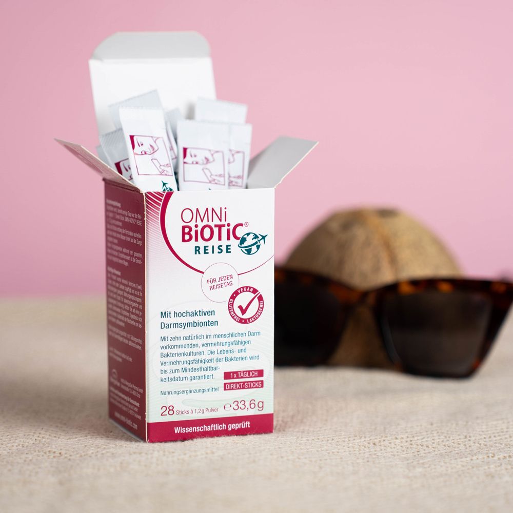 Geöffnete Verpackung von OMNi-BiOTiC REISE Direkt-Sticks. Sticks sind sichtbar. Hintergrund: Kokosnuss und Sonnenbrille.