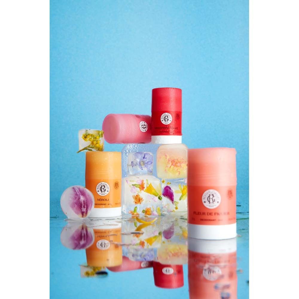 Mehrere Deodorant-Sticks, rosa und orange, auf Eiswürfeln mit Blumen. Spiegelung auf einer blauen Oberfläche.