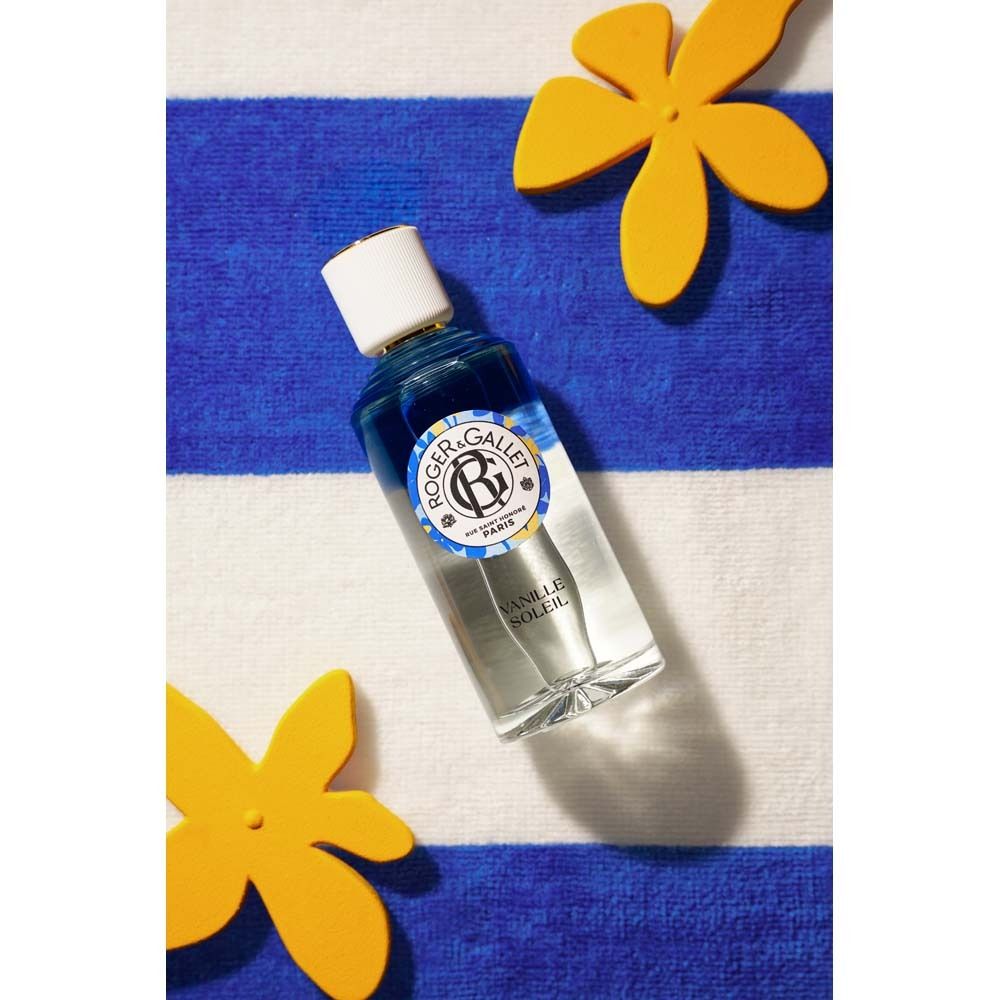 Flakon auf blau-weiß gestreiftem Handtuch, gelbe Blüten. Flakon mit weißem Deckel, Logo und Schriftzug "Vanille Soleil".