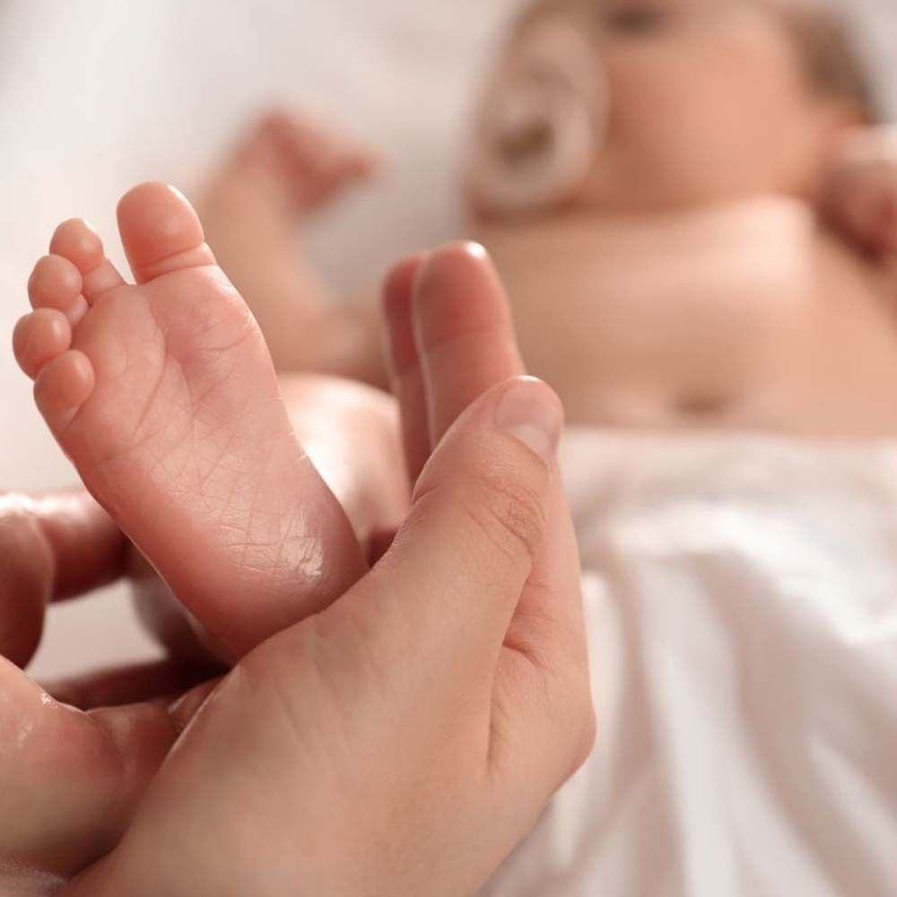 Nahaufnahme eines Babyfußes in einer Hand. Der Fuß ist leicht geölt.