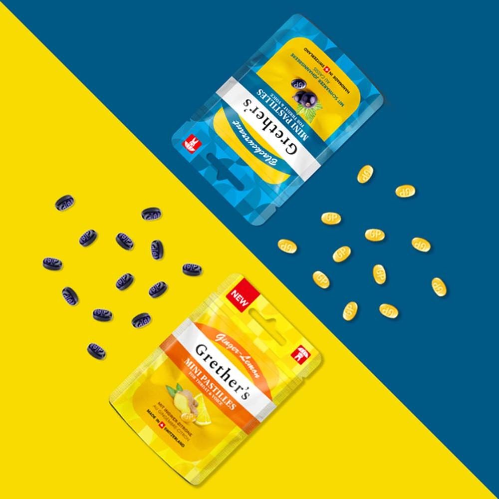 Zwei Packungen Grether's Mini Pastillen. Eine gelb, eine blau. Pastillen liegen daneben. Aufdruck: Ginger-Lemon und Blaubeere.