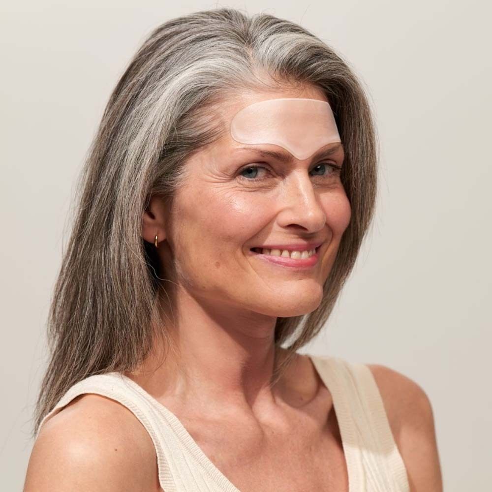 Frau mit Stirn Pad auf der Stirn. Transparentes Pad. Graue Haare. Beige Oberteil.