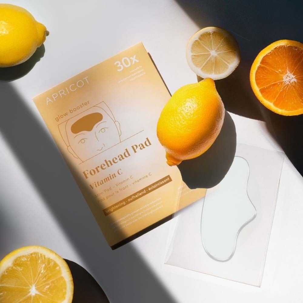 Stirn Pad mit Vitamin C und Verpackung. Zitronen und Orange daneben. Text: APRICOT, Forehead Pad, 30x.