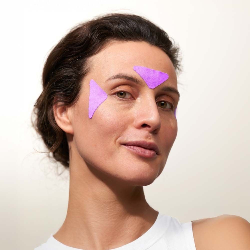 Frau mit zwei lila Facial Patches auf der Stirn. Produktname nicht sichtbar.