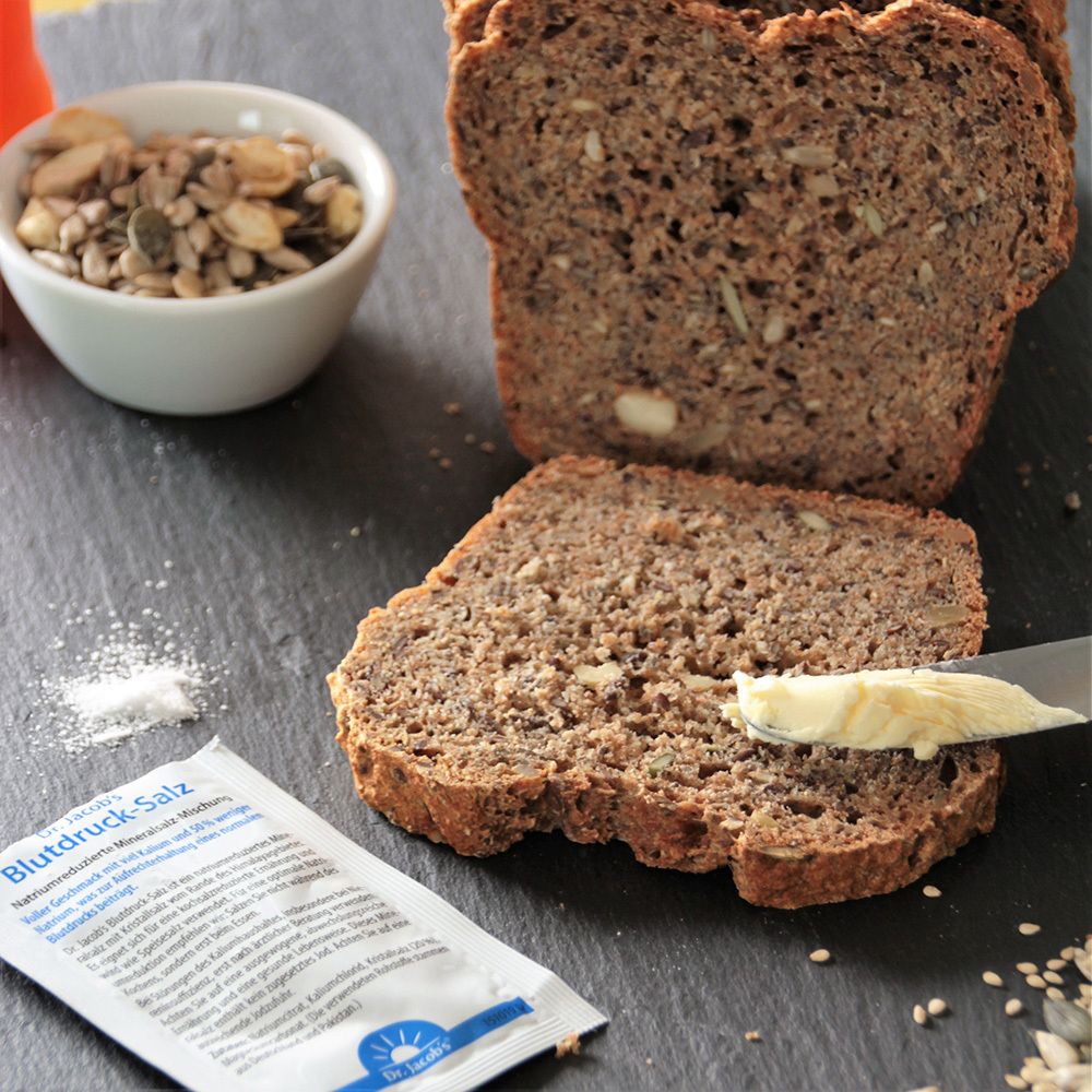 Brot mit Butter und Dr. Jacob's Blutdruck-Salz. Kleines Tütchen Salz. Auf schwarzem Untergrund.