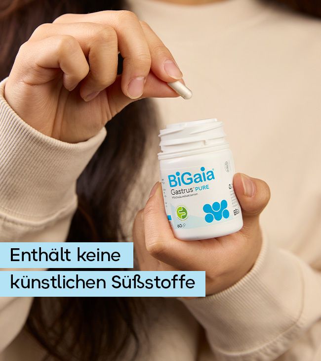 Eine Hand hält eine Kapsel und eine weiße Flasche BiGaia Gastrus Pure mit blauen Symbolen.