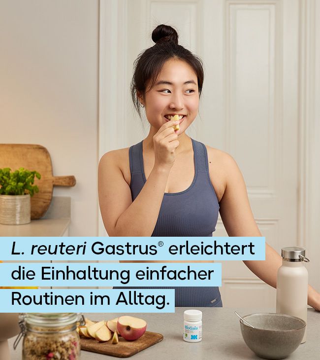 Junge Frau isst Obst in der Küche neben einem Glas mit Müsli und einer Flasche.