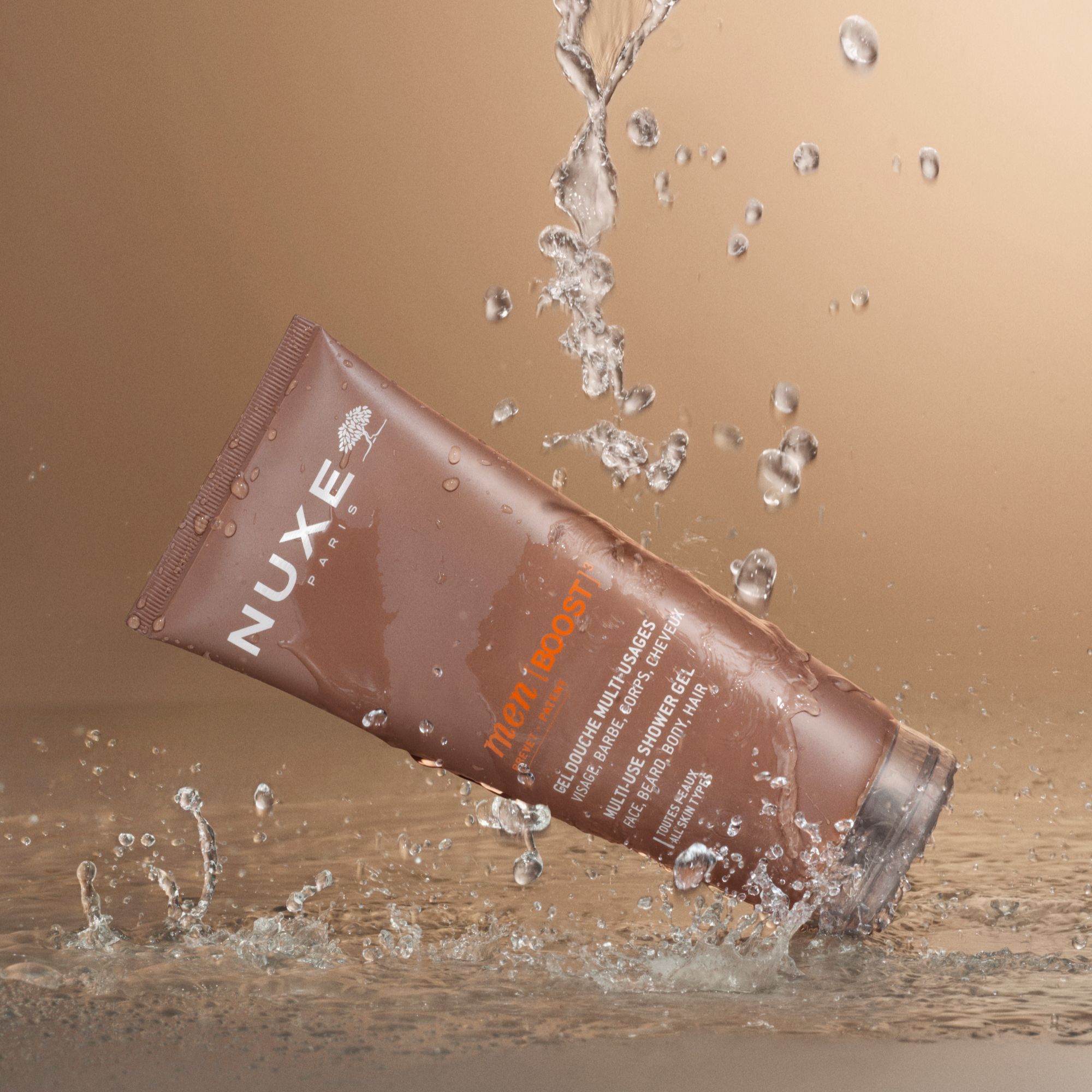 NUXE PARIS men [BOOST]³ Duschgel-Tube im Wasser. Wasser spritzt. Produkt im Fokus.