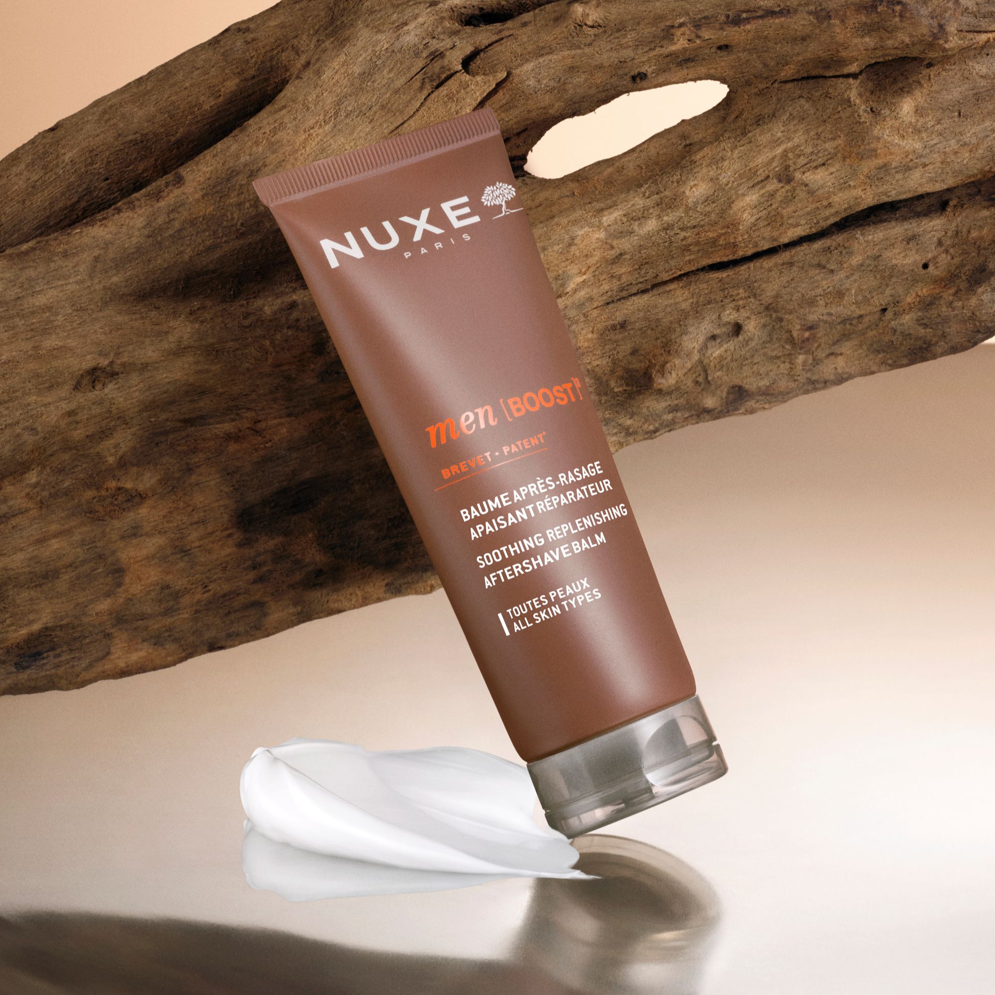 Braune Tube NUXE Men [BOOST]³ After-Shave-Balsam auf Holz und Creme. Text: Baume après-rasage, Soothing Replenishing Aftershave Balm. Für alle Hauttypen.
