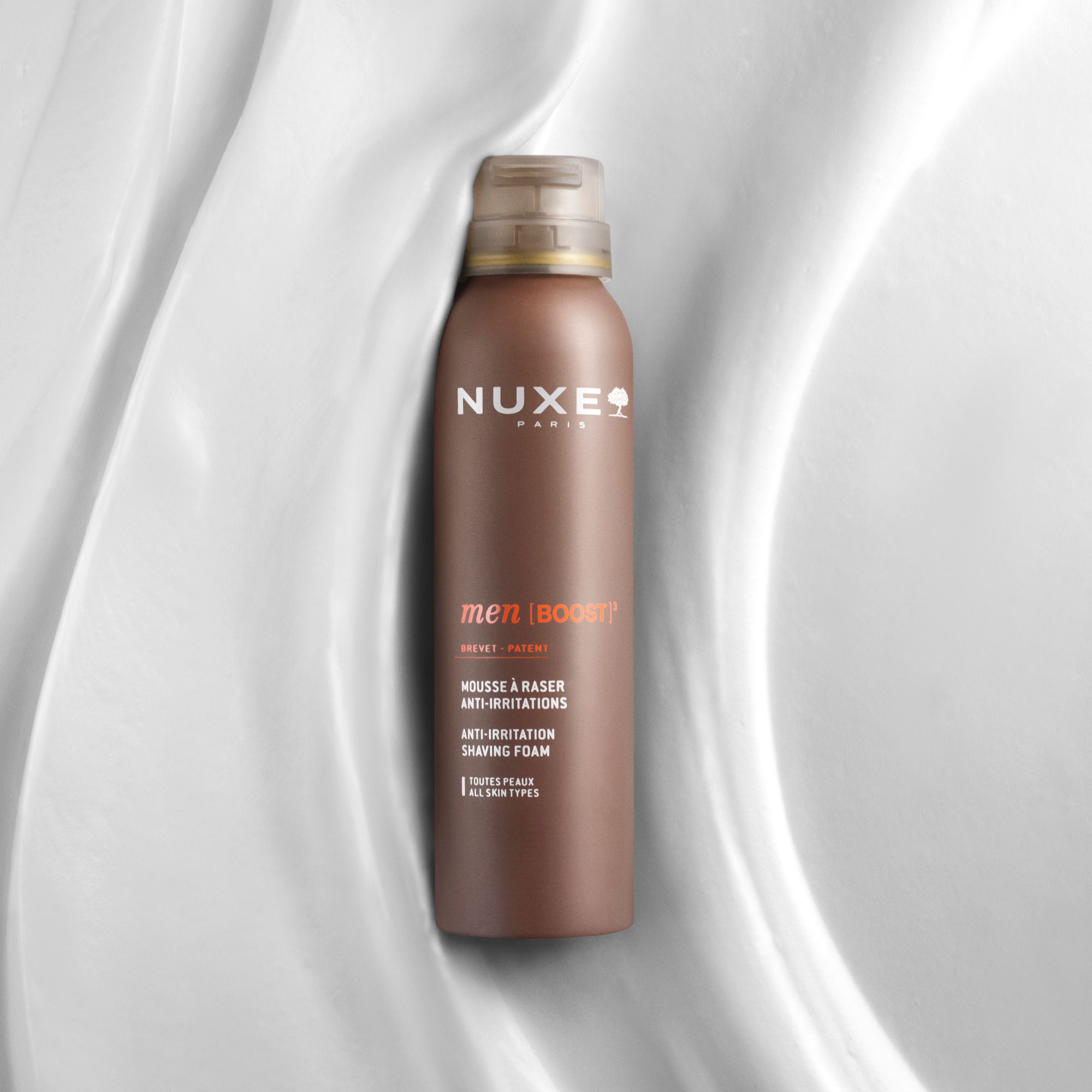 Braune Sprühflasche mit braunem Deckel. Aufschrift: NUXE PARIS, men [BOOST]³, Mousse à raser, Anti-Irritations, 150 ml.