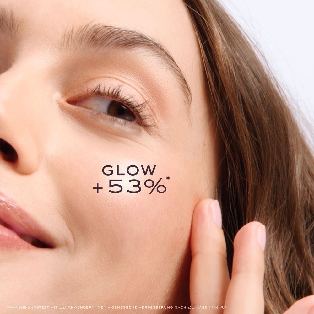 Nahaufnahme eines Gesichts. Auf der Wange steht: GLOW +53%*. Die Hand berührt die Haut.