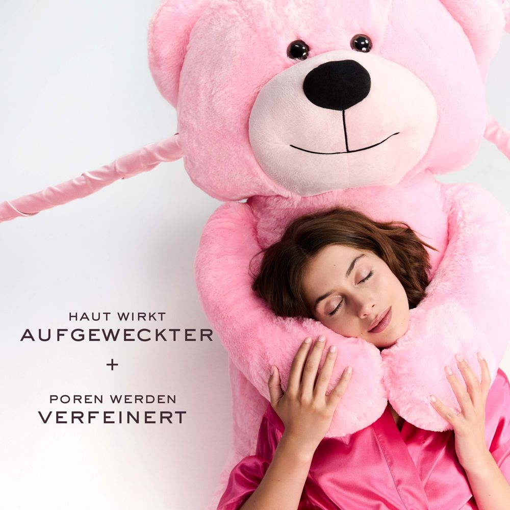 Frau mit geschlossenen Augen, umarmt einen rosa Teddybären. Text: Haut wirkt aufgeweckter + Poren werden verfeinert.