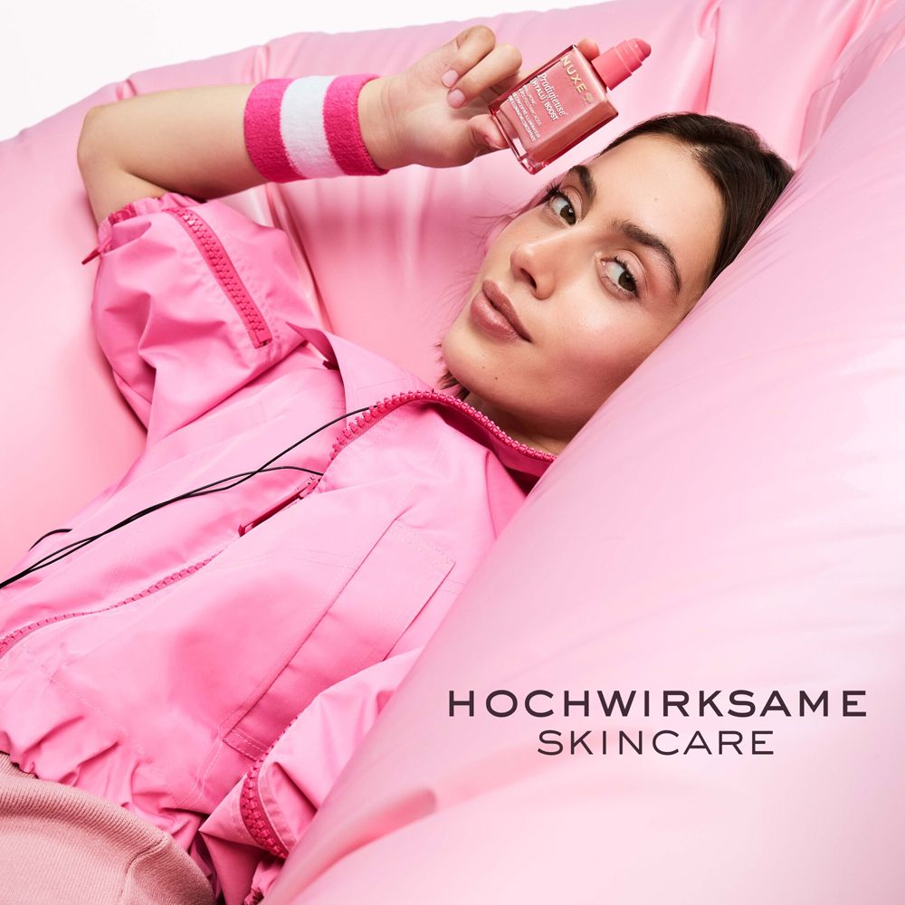 Frau liegt auf einem rosa Kissen und hält eine Serumflasche. Text: HOCHWIRKSAME SKINCARE.