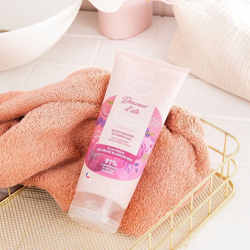 Rosa Tube mit LAINO-Logo und "Gel Douche Hydratant" auf einem Handtuch und in einem Korb. Hintergrund: Bad.