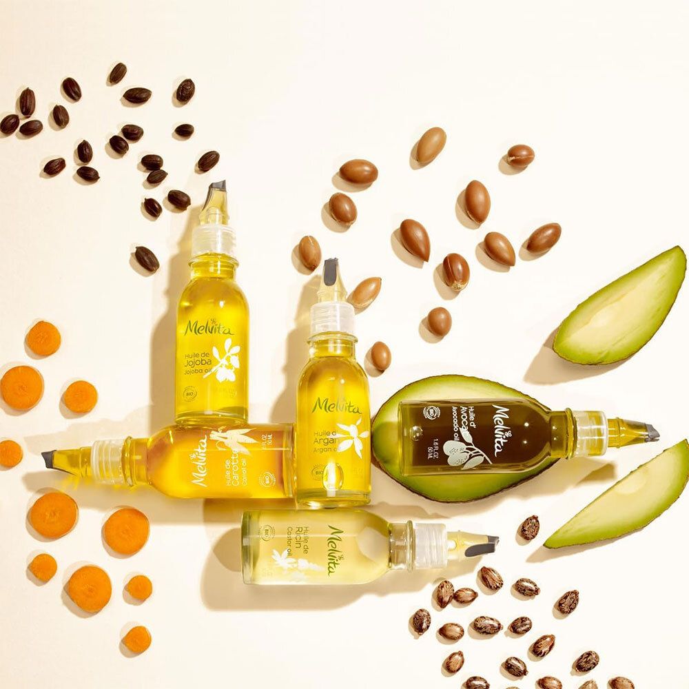 Mehrere Flaschen mit gelber Flüssigkeit, umgeben von Samen und Früchten. Aufschrift Melvita.