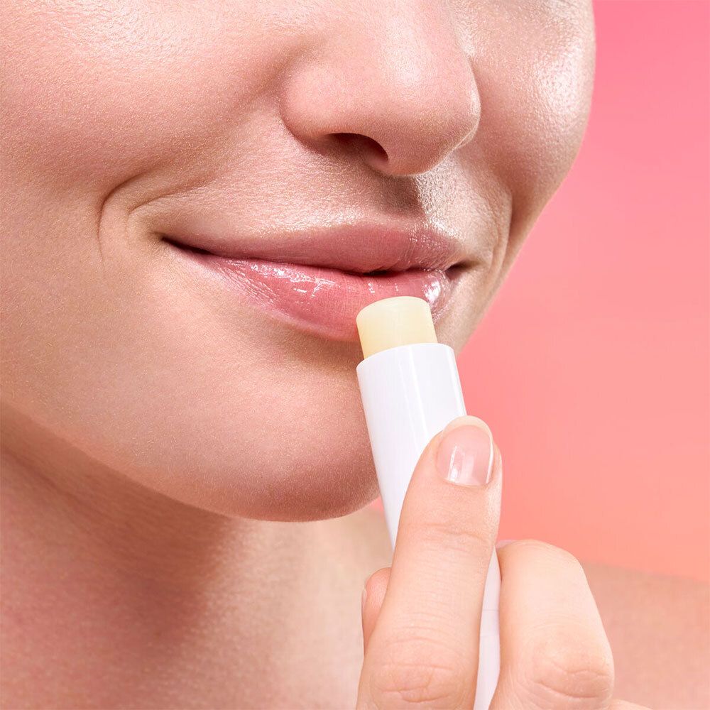 Person trägt Lippenbalsam auf. Weißer Stift, gelbe Spitze. Lippen glänzend.