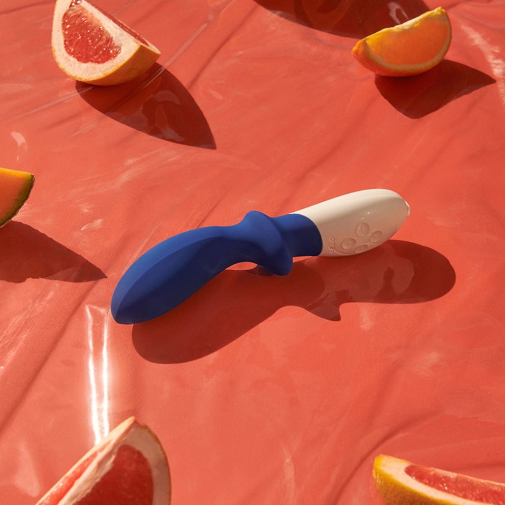 Blau-weißes Massagegerät auf rotem Hintergrund mit Grapefruit- und Orangenscheiben.