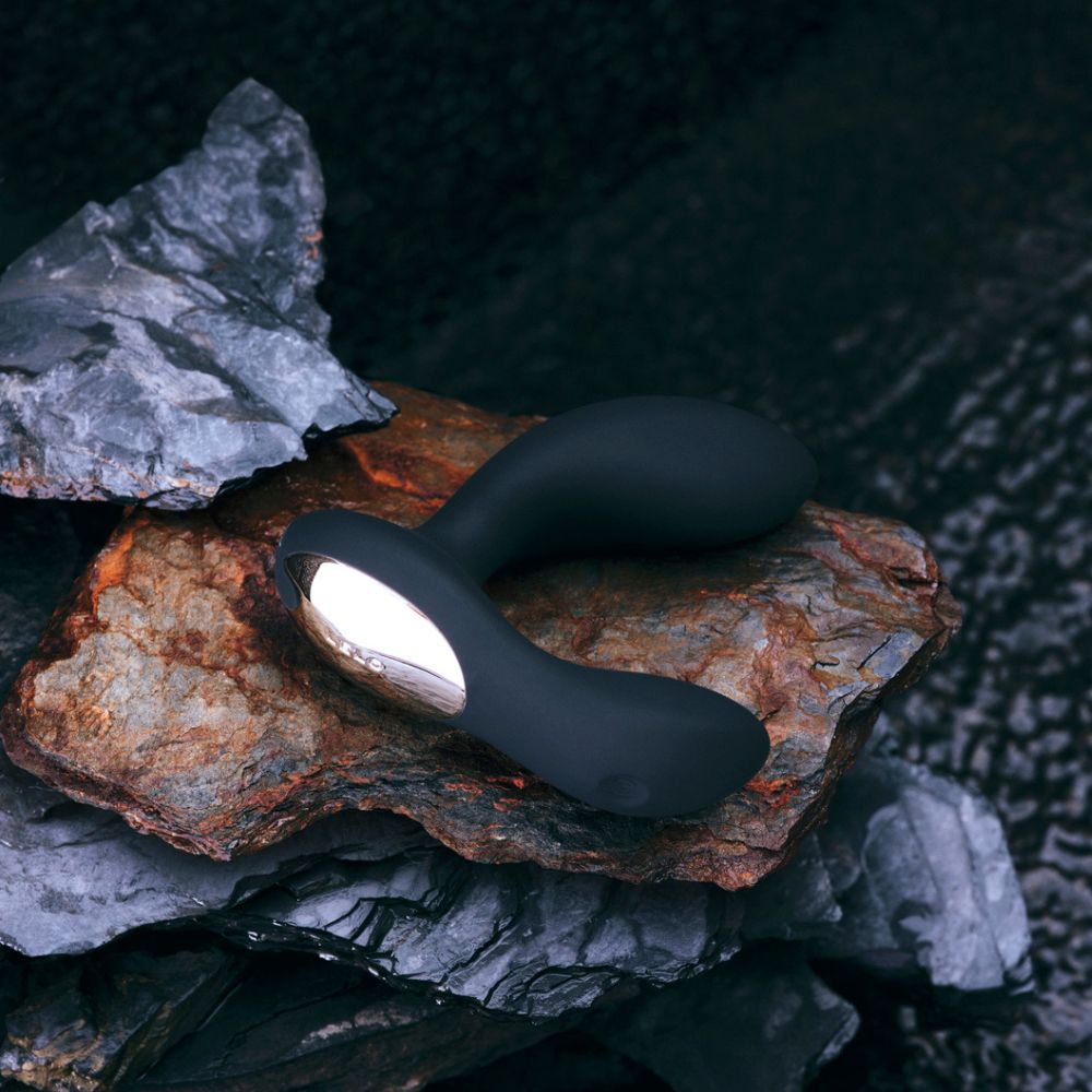 Schwarzer Vibrator auf Steinen. Goldfarbene Basis. Glatte Oberfläche.