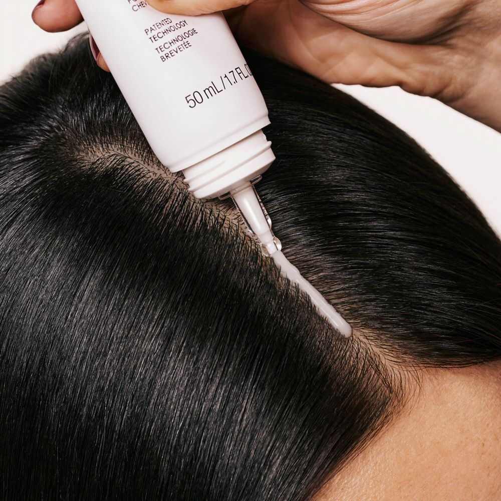 Anwendung von Olaplex N°.0.5 auf der Kopfhaut. Tube mit Applikator. Schwarzes Haar.