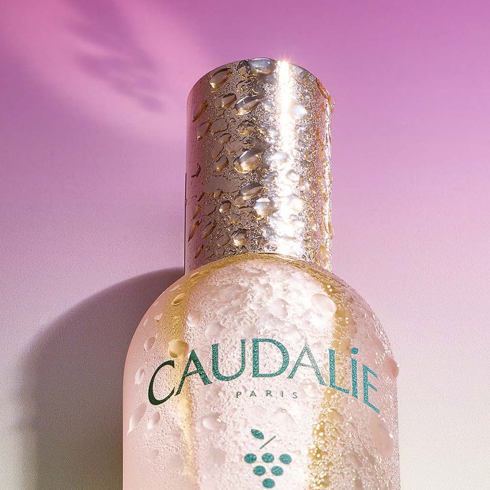 Hand sprüht Caudalie Eau de Beauté. Flasche mit silbernem Deckel. Text: Caudalie, Beauty Elixir.