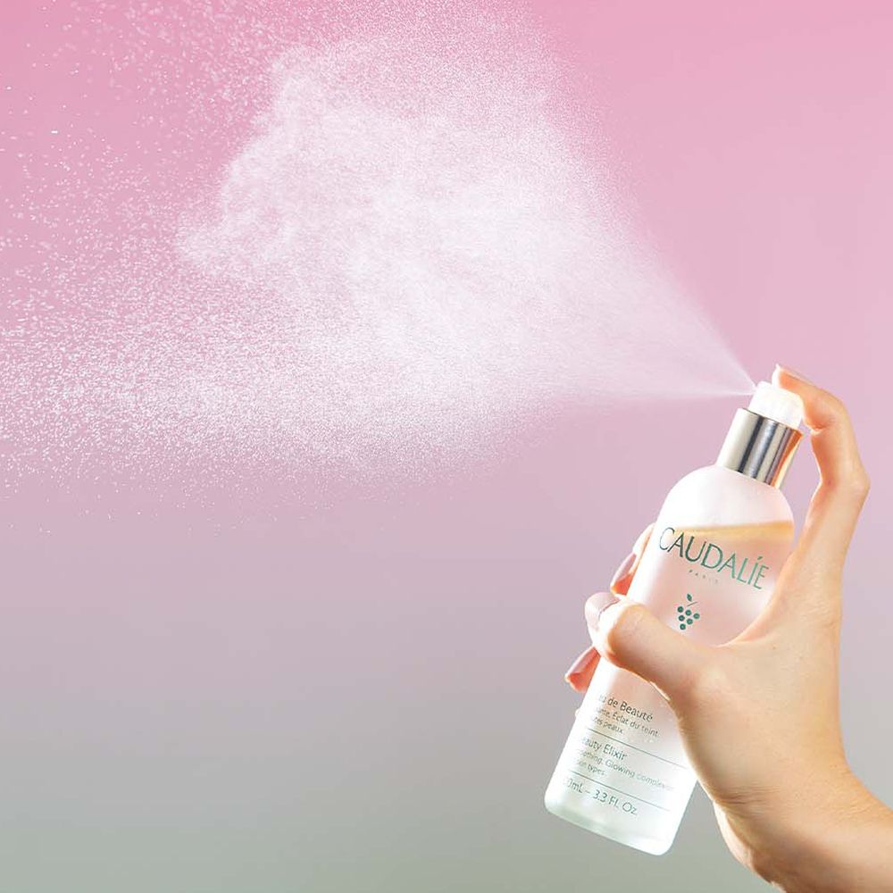 Caudalie Eau de Beauté Flasche. Farbverlauf von Grün nach Rosa. Silberner Deckel. Text: Beauty Elixir.