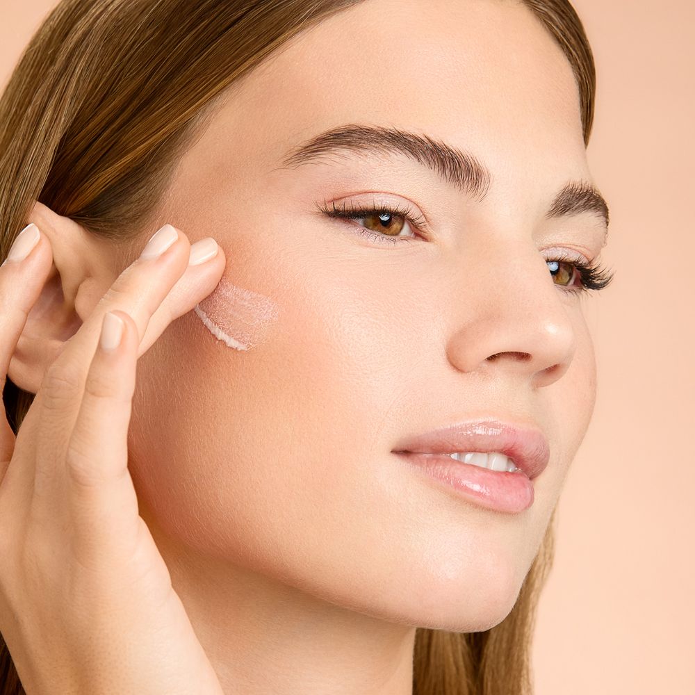 Frau trägt Produkt auf. Hautpflegeprodukt wird auf die Wange aufgetragen. Beige Hintergrund.