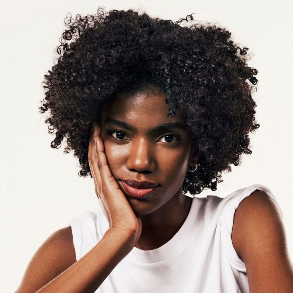Porträt einer Frau mit lockigem Haar. Sie berührt ihre Wange mit der Hand.