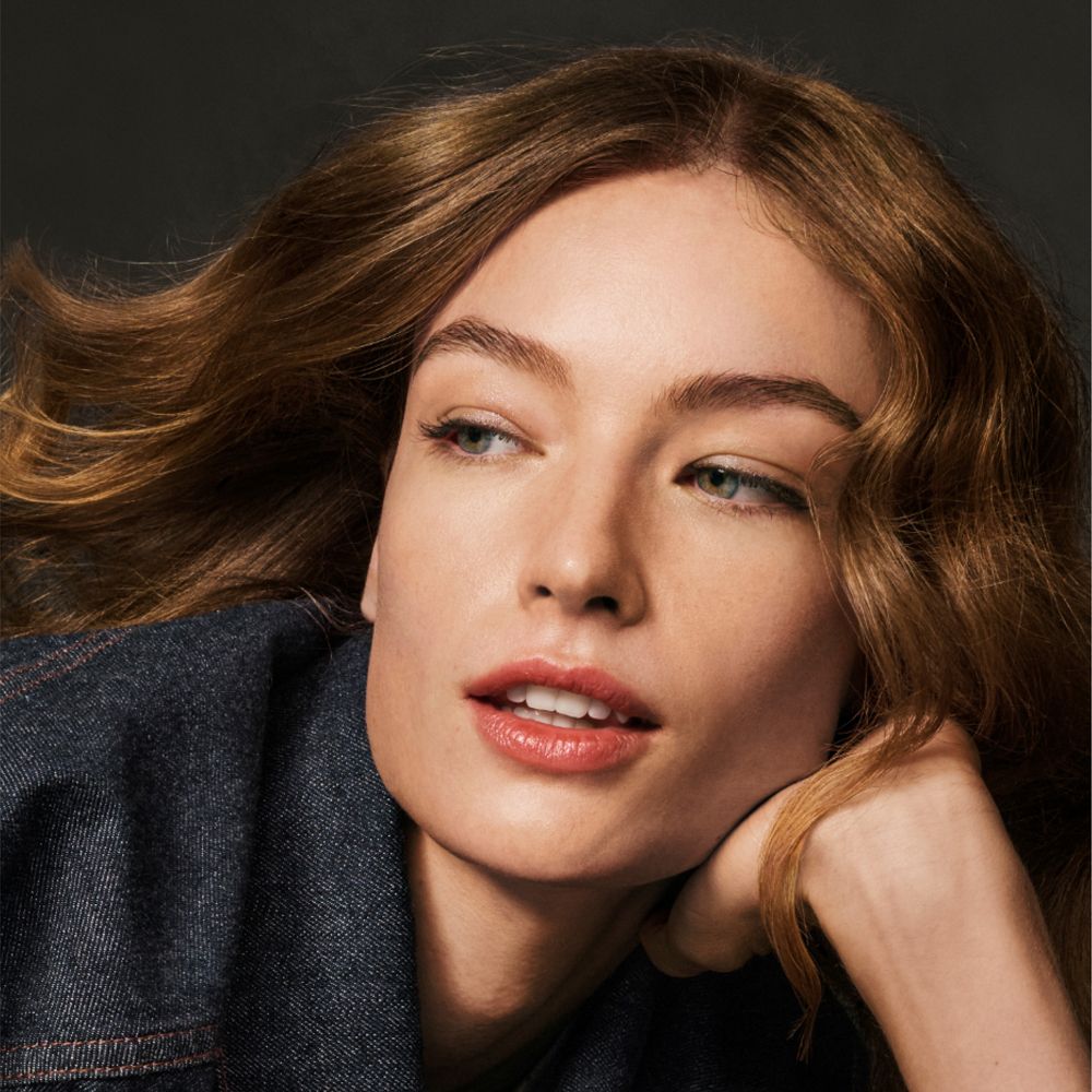 Porträt einer Frau mit welligem, braunem Haar. Sie schaut zur Seite, trägt Jeansjacke.